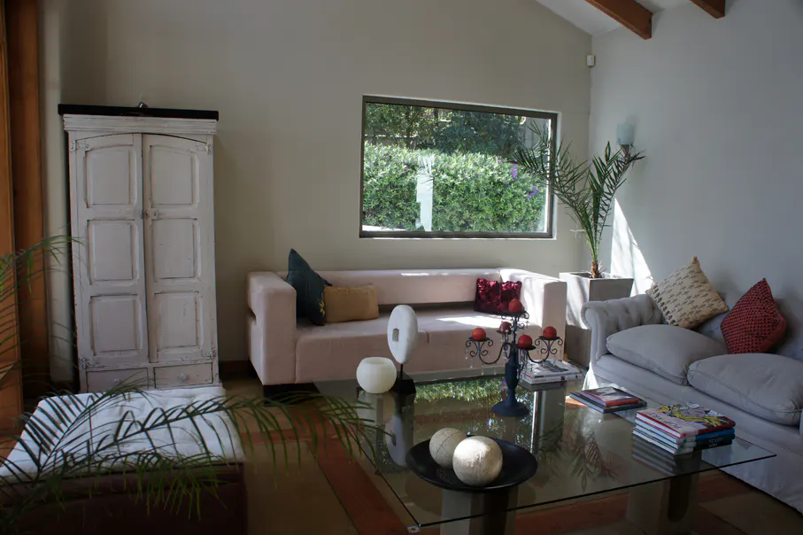 Living room with a pink sofa, a gray sofa, a glass table, and a white cabinet. A window overlooks a green garden.