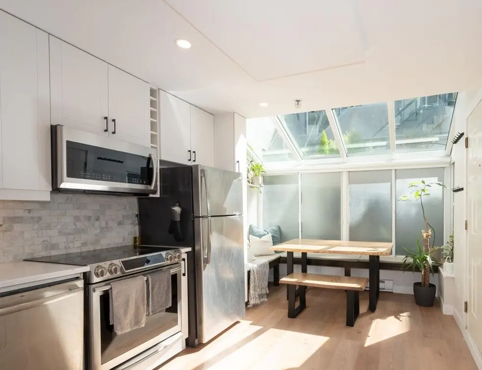 Bright kitchen with stainless steel appliances, white cabinets, and a dining area with skylights.