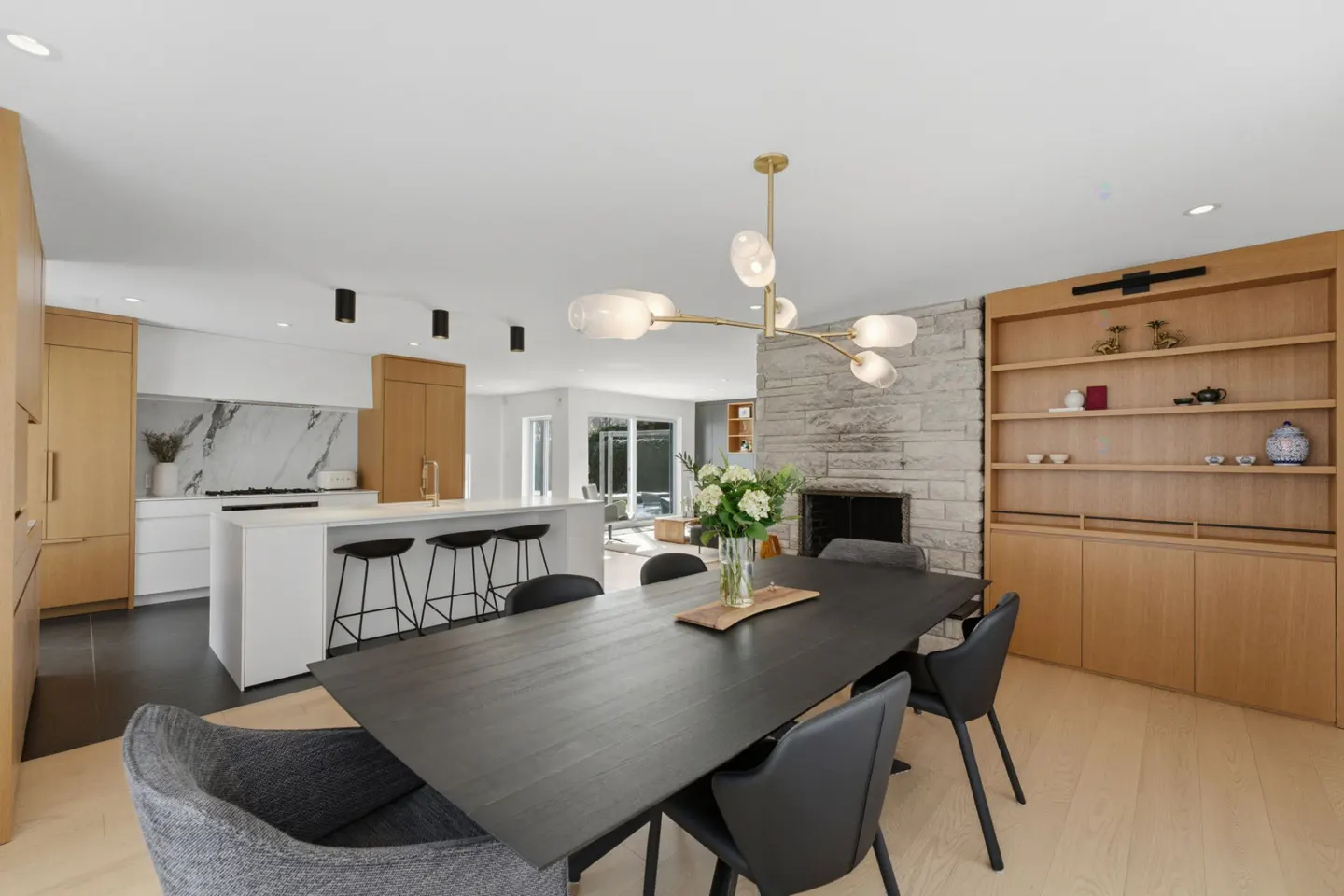 Open-concept home with a black dining table, modern chandelier, and kitchen island with marble backsplash.