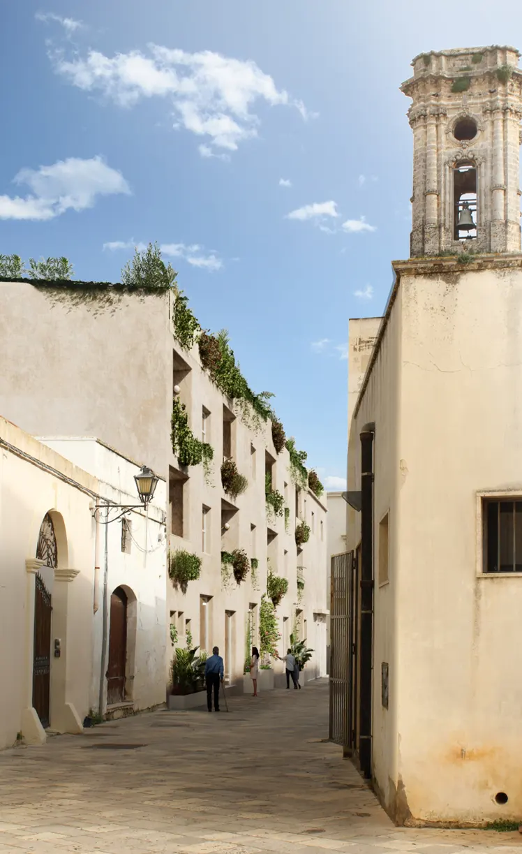Street view of white buildings with greenery, people walking, and a bell tower under a blue sky.
