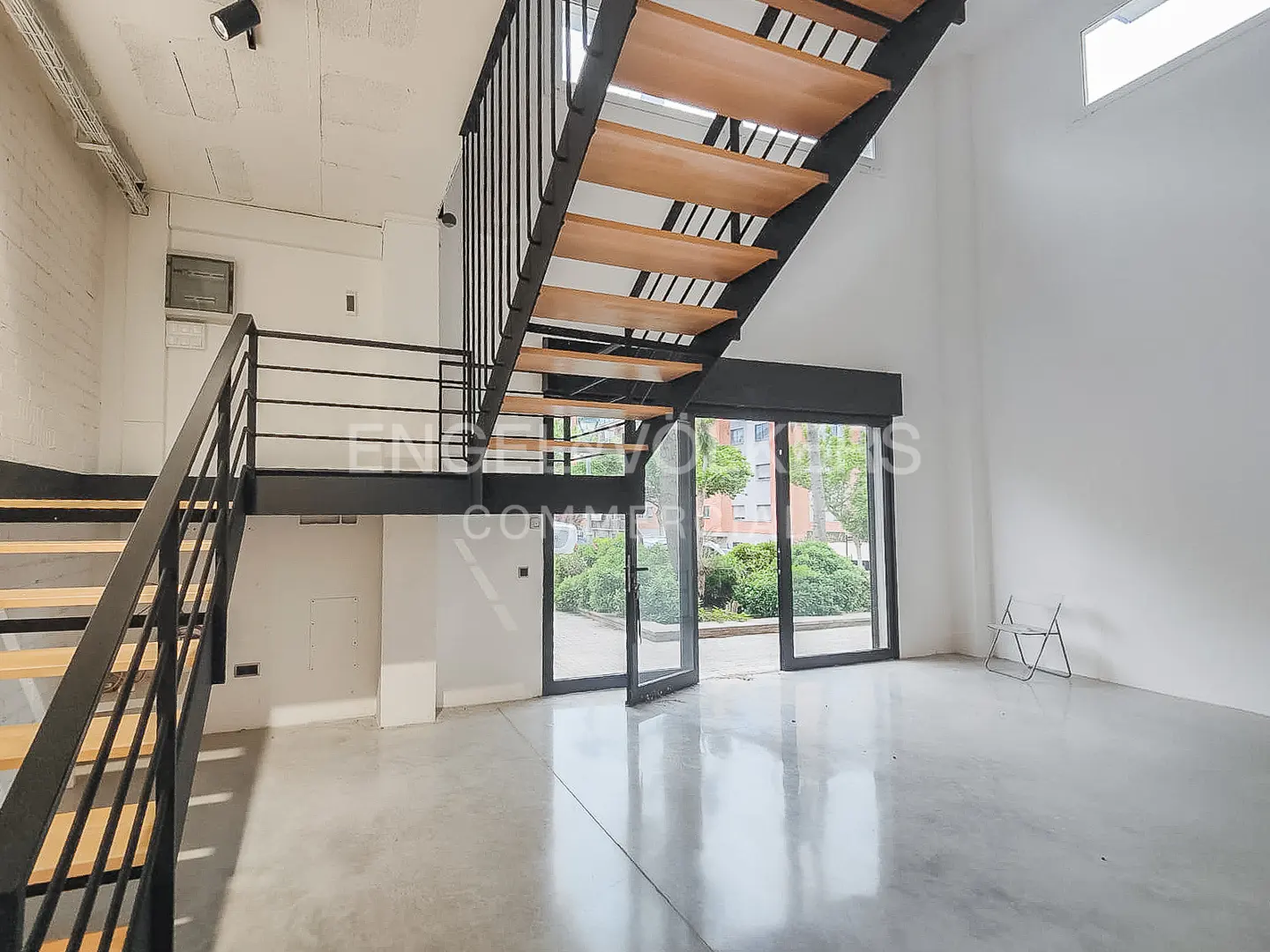 Modern industrial interior with a black metal staircase, wooden steps, polished concrete floors, and glass patio doors.