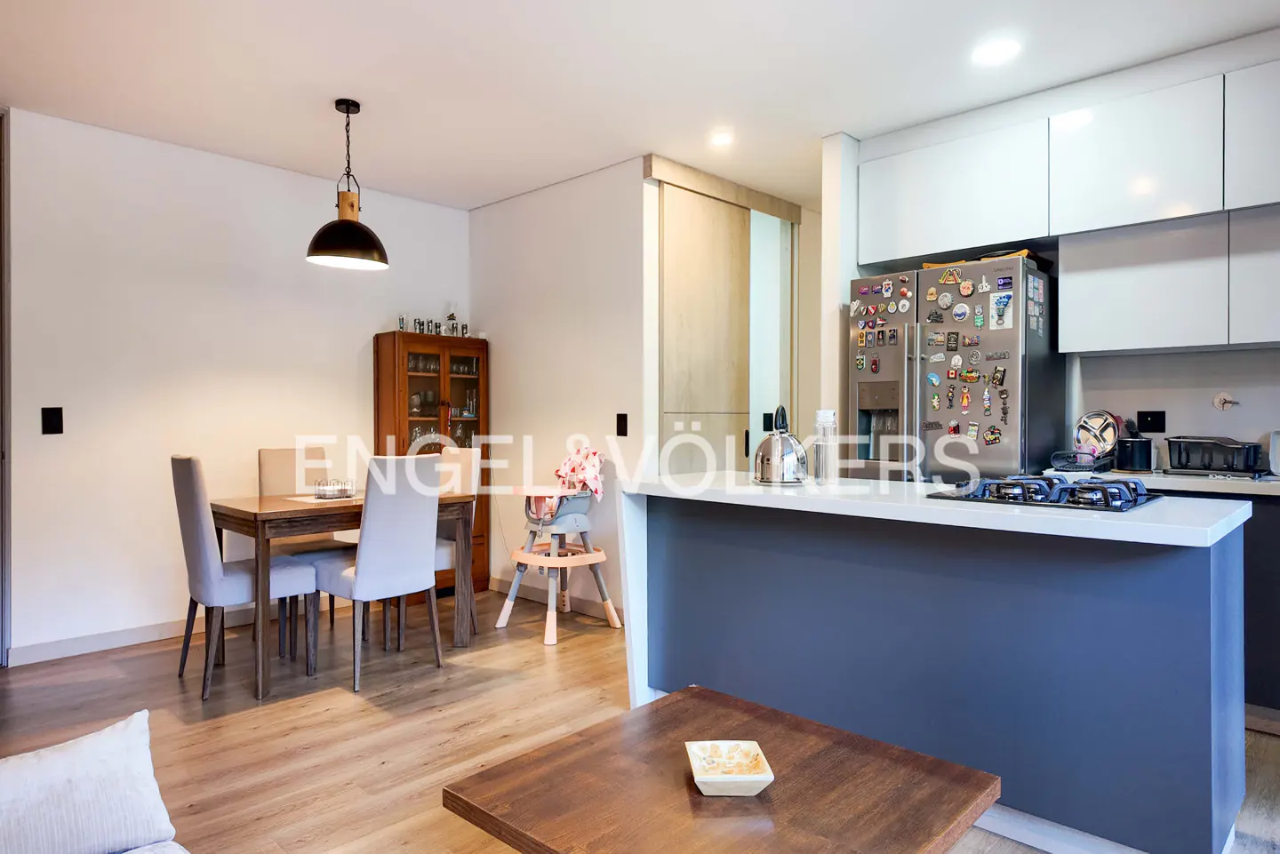 A modern apartment interior with a dining table, chairs, and a kitchen island with white countertops.