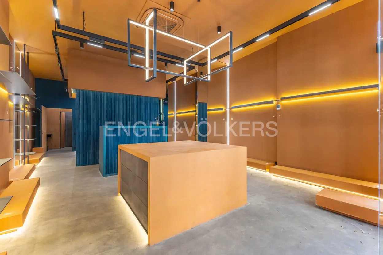 Interior of a retail space with orange walls, blue accents, and modern lighting fixtures. A large display table sits in the center.
