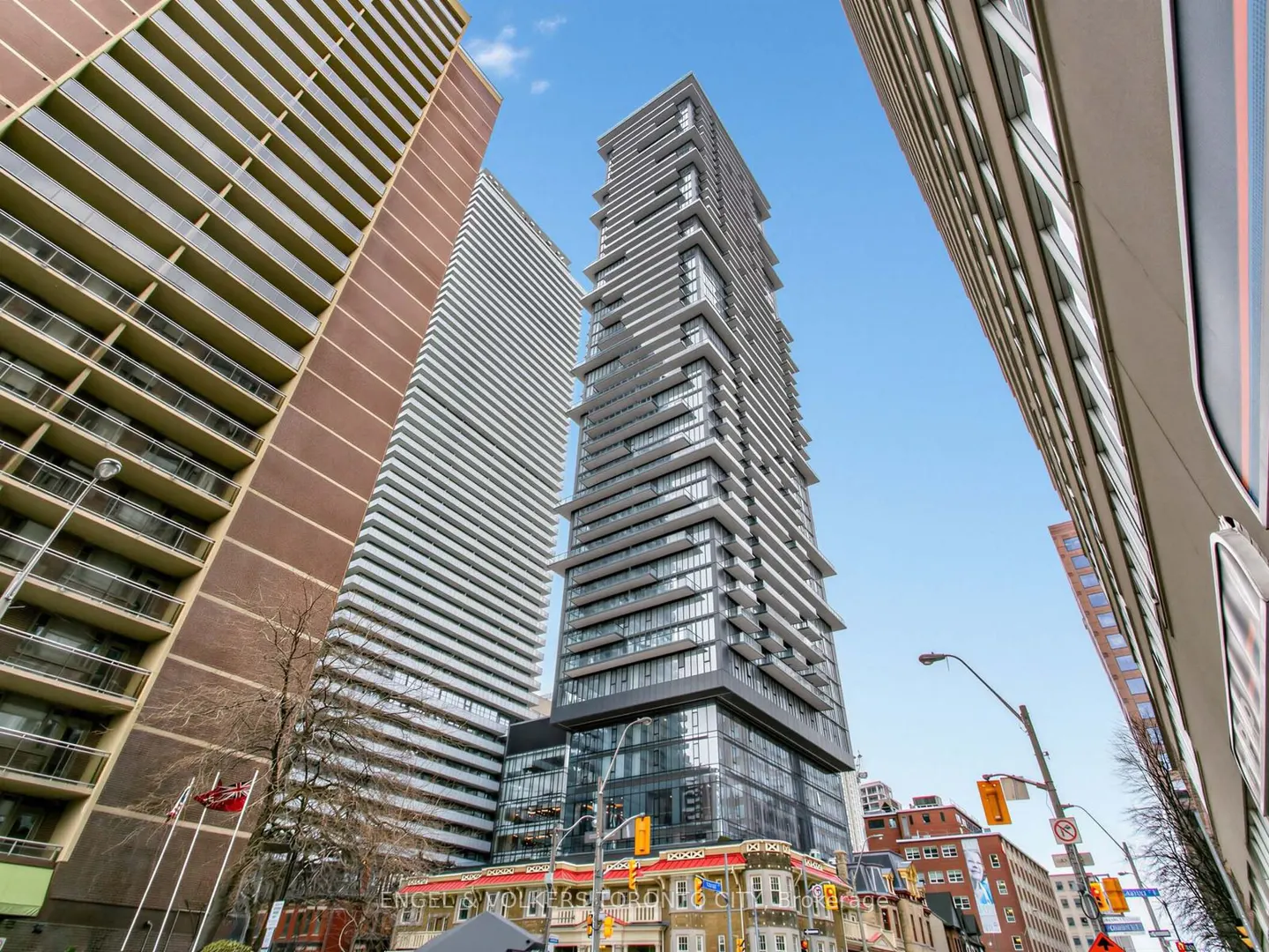 View of a tall, modern gray condo building with horizontal lines, surrounded by other buildings, under a blue sky.