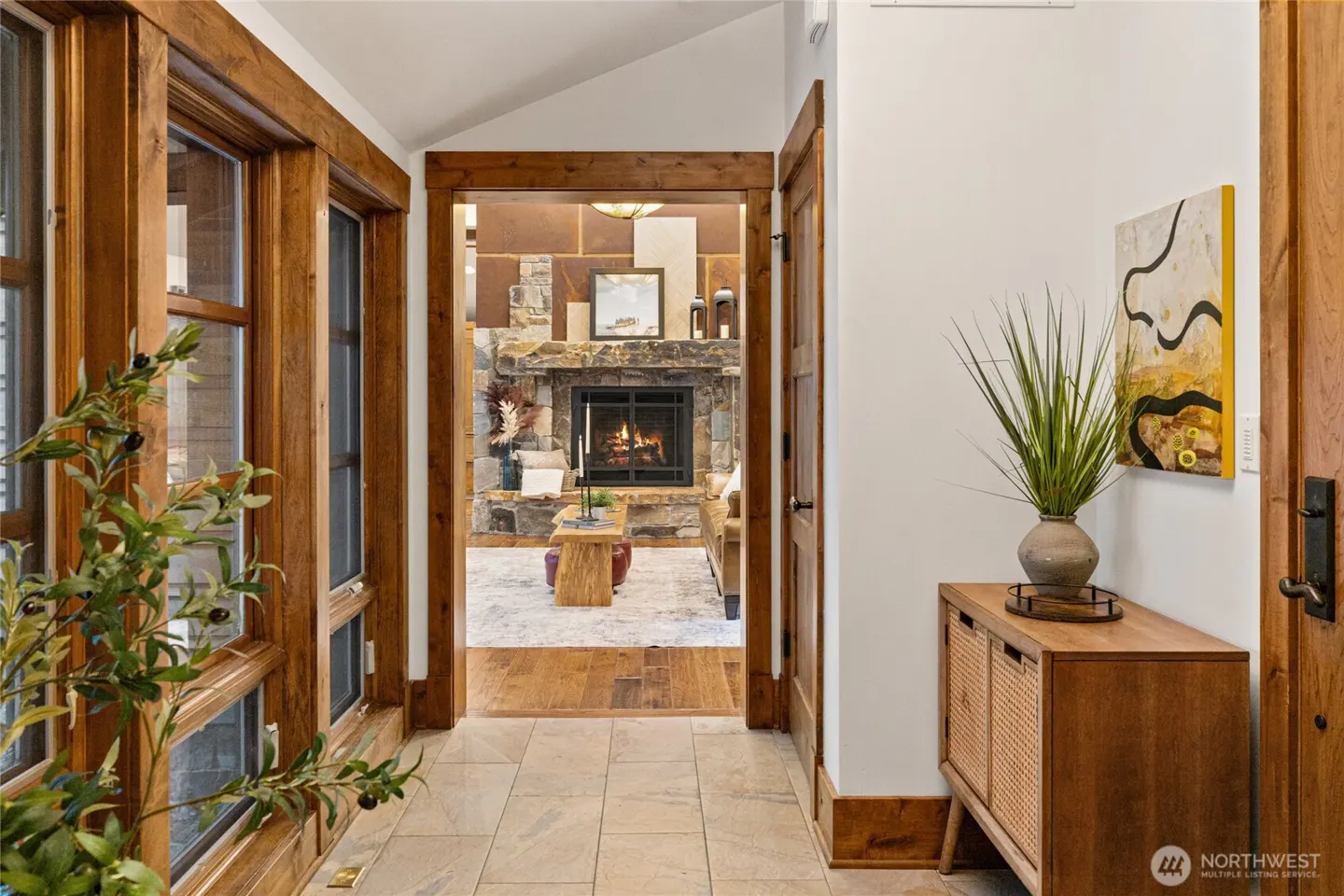 Entryway with tile floor, wooden console table, and a view into a cozy living room with a stone fireplace.