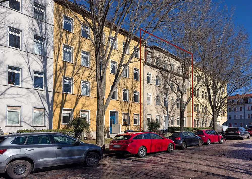 A street view of a yellow and white apartment building with parked cars and bare trees.
