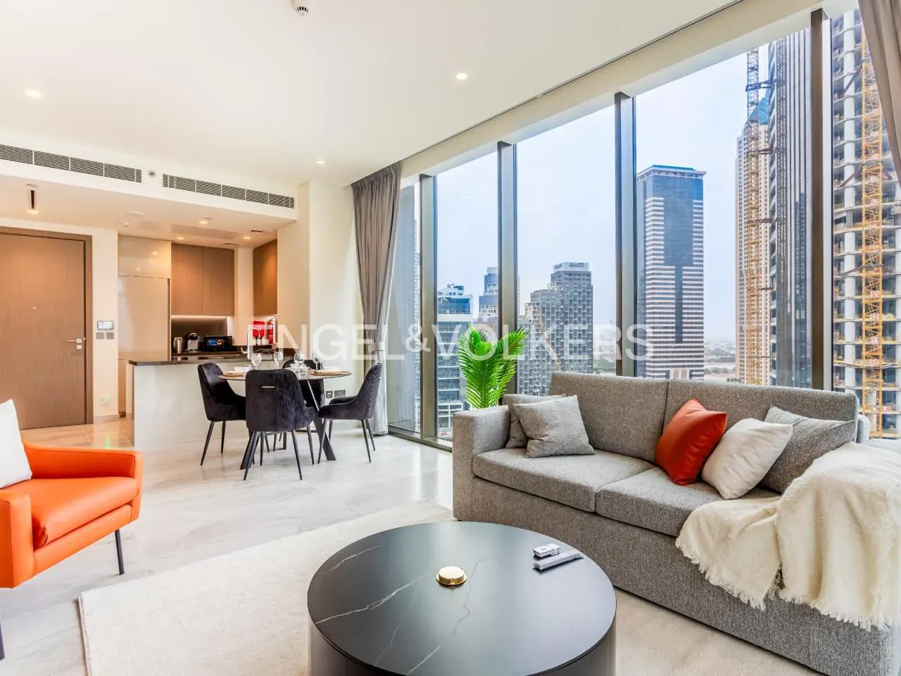 A modern apartment interior with a gray sofa, orange chair, and city view through large windows.