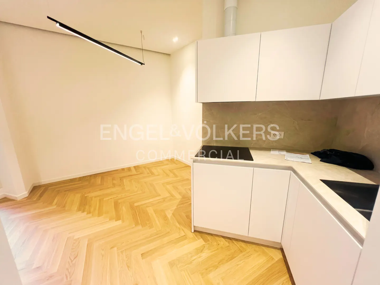 Bright, modern kitchen with white cabinets, light wood herringbone floors, and a long, linear black light fixture.