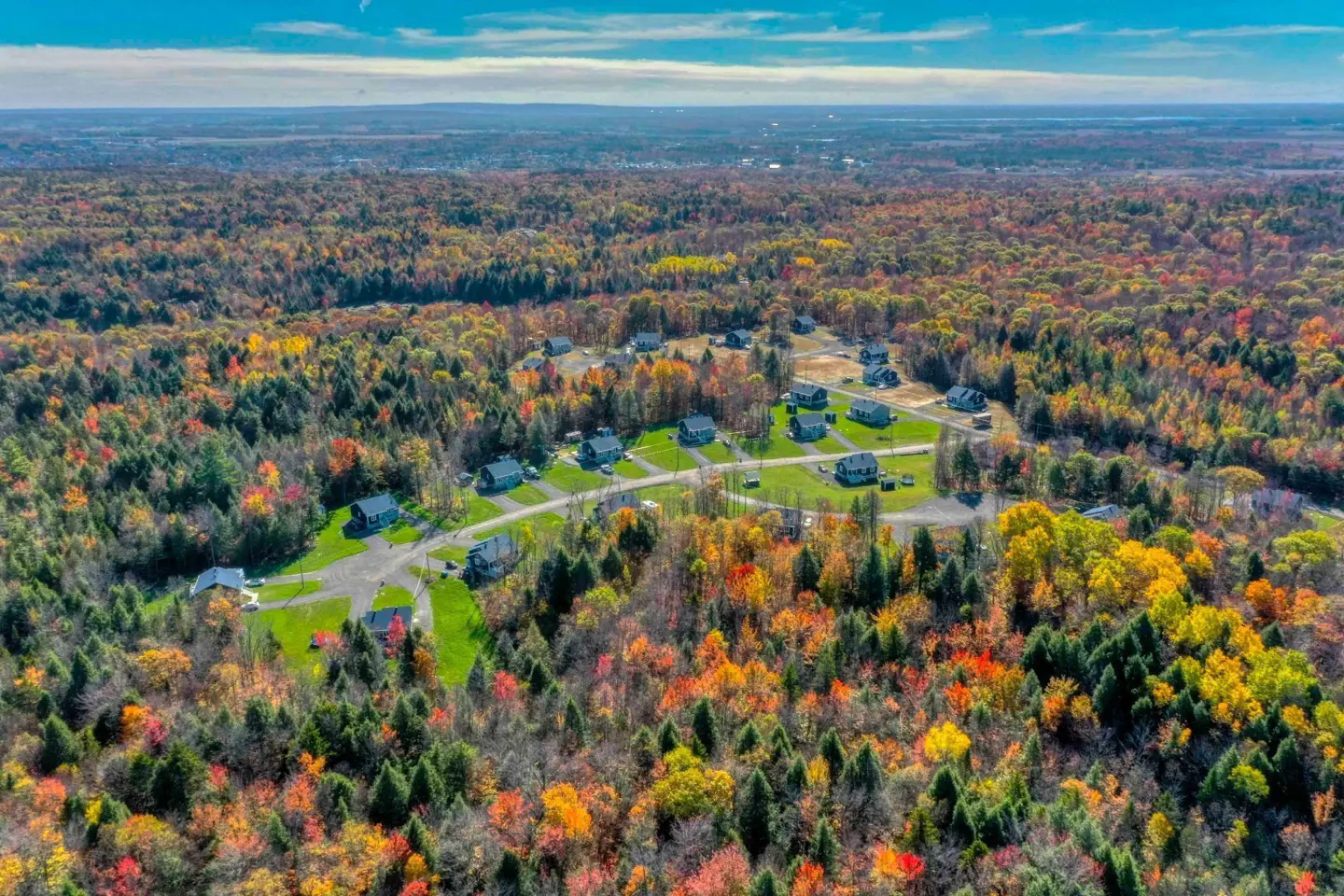 Aerial view of a neighborhood nestled in a colorful autumn forest under a blue sky.