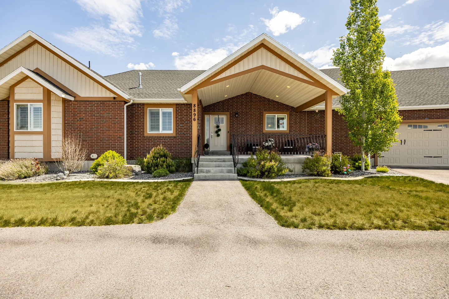 Red brick house with a covered porch, white trim, and a concrete walkway leading to the front door. Green lawn and blue sky.