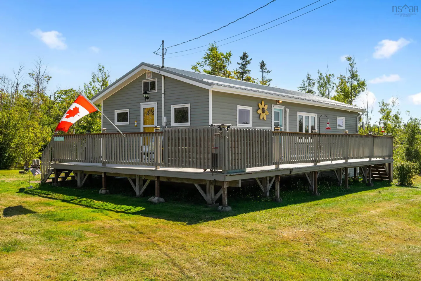 A gray house with a large deck and a Canadian flag on a sunny day.