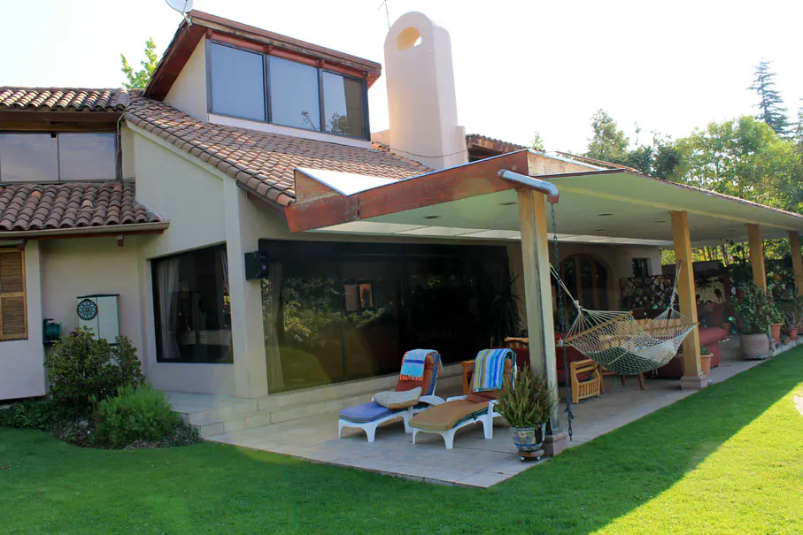 Beige house with a red tile roof and a covered patio with lounge chairs and a hammock.