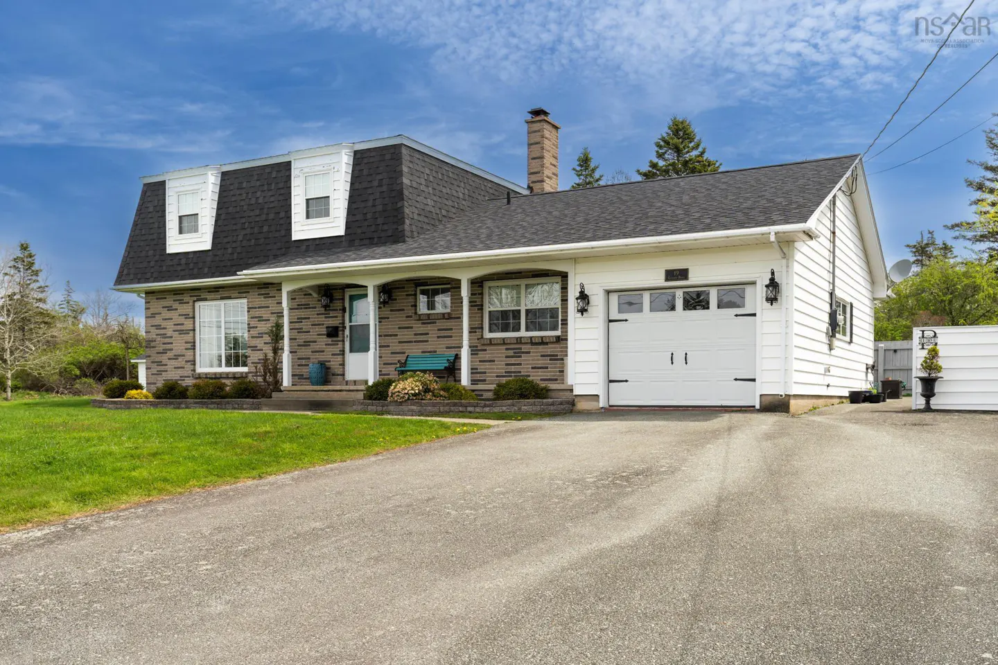 Exterior view of a one-story house with a brick facade, white garage door, and a dark gray roof. A green lawn and driveway are in front.