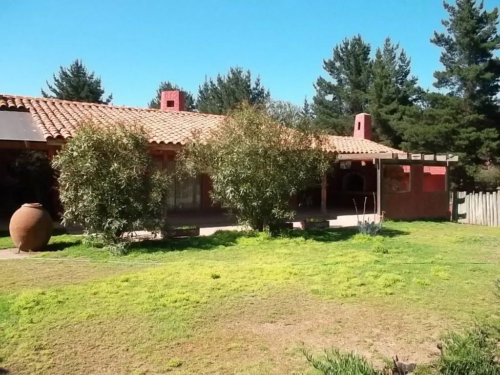 Exterior view of a red house with a clay tile roof, green lawn, trees, and a large clay pot.