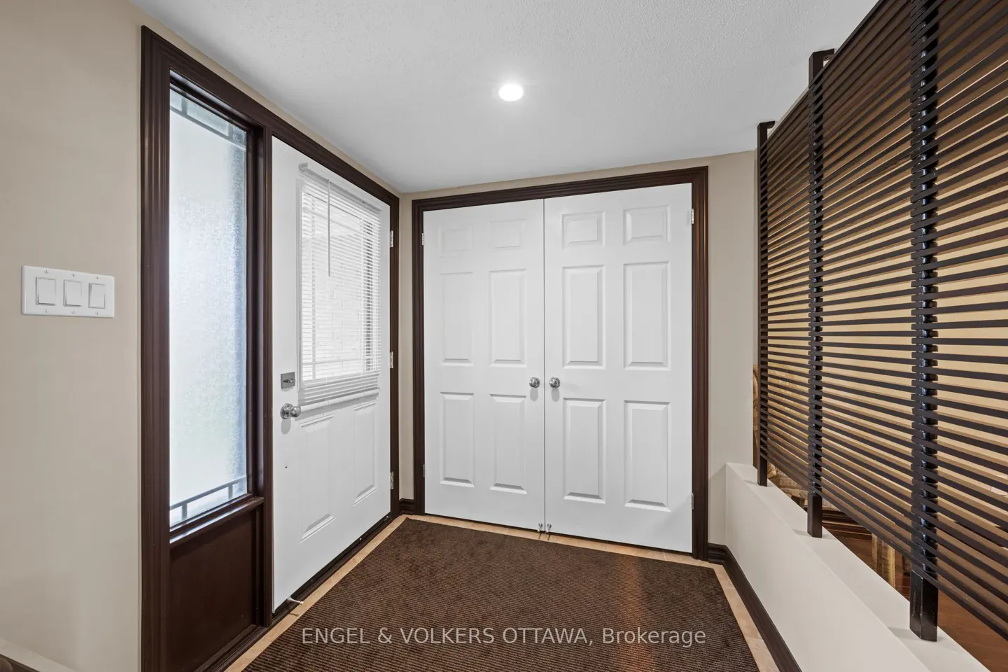A foyer with a white front door, a frosted glass window, and a brown frame. There are white double doors and a brown slatted wall.