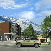 Modern brown and white building with a tan SUV parked in front. Snow-capped mountains are in the background under a blue sky.