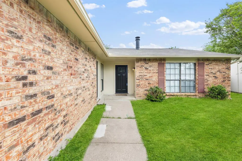 Exterior of a brick home with a black front door, brown shutters, and a green lawn.