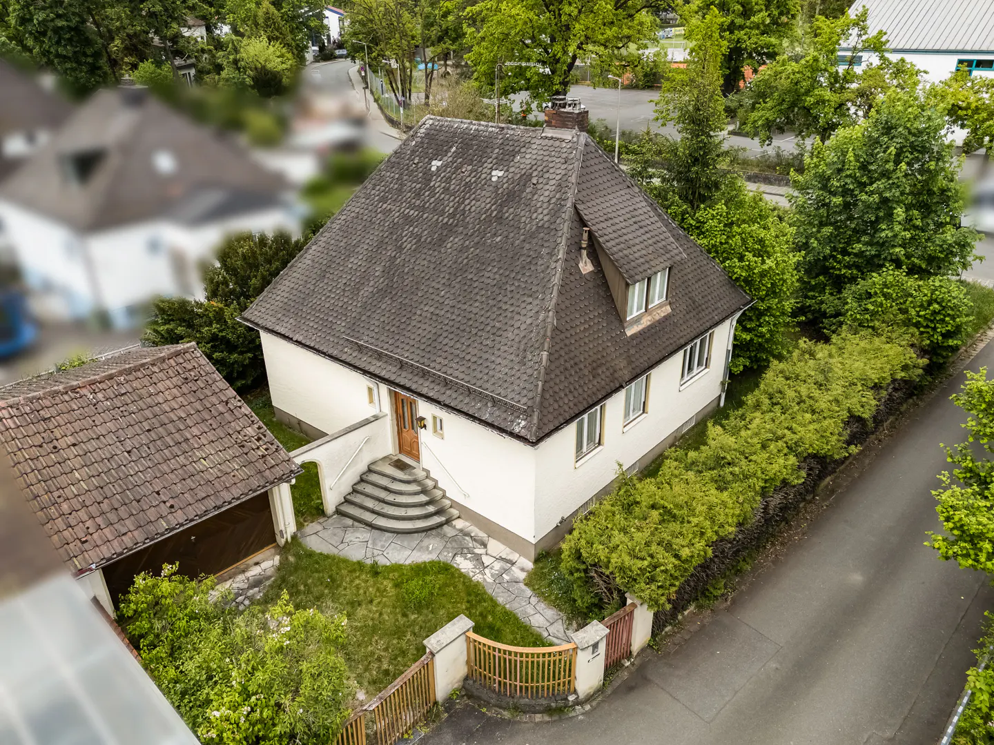Aerial view of a white house with a gray roof, stone steps to the front door, and a detached garage.