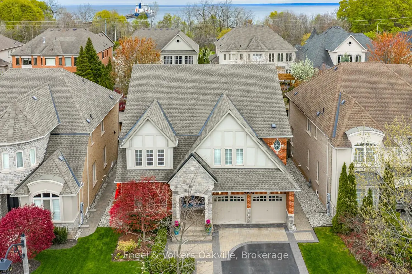 Aerial view of a two-story house with a gray roof, white trim, and a two-car garage, surrounded by green lawn and other houses.