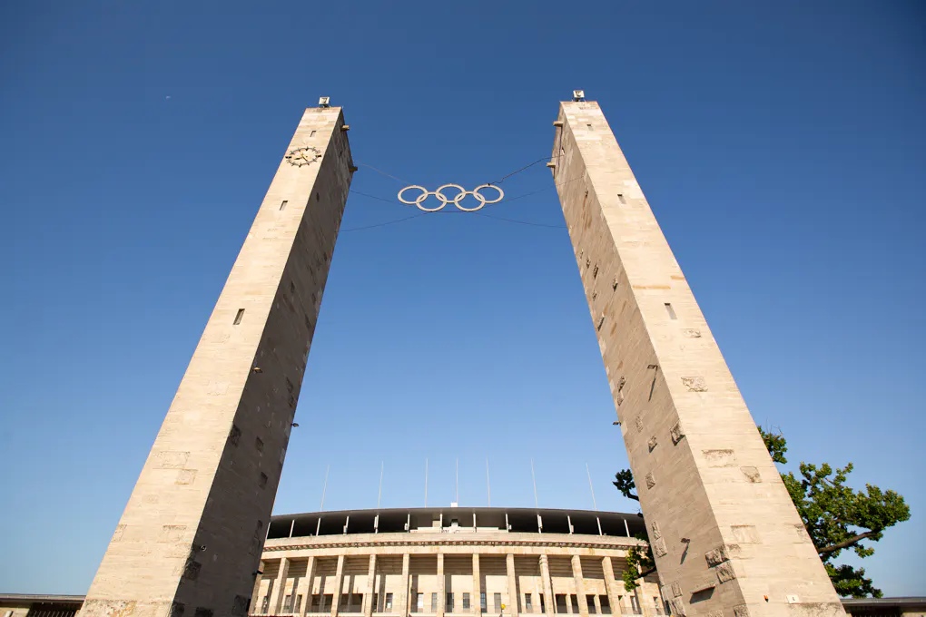 View of the Olympic Stadium in Berlin, Germany, with the Olympic rings suspended between two tall towers.
