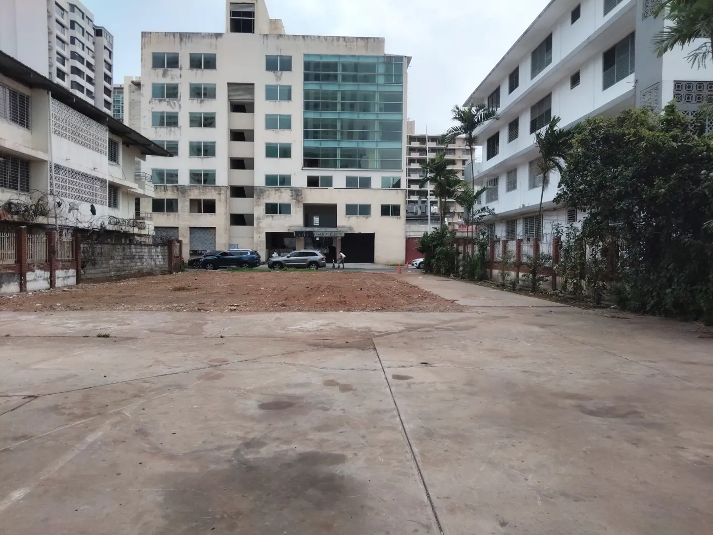 A vacant lot with a concrete surface, surrounded by buildings and parked cars.