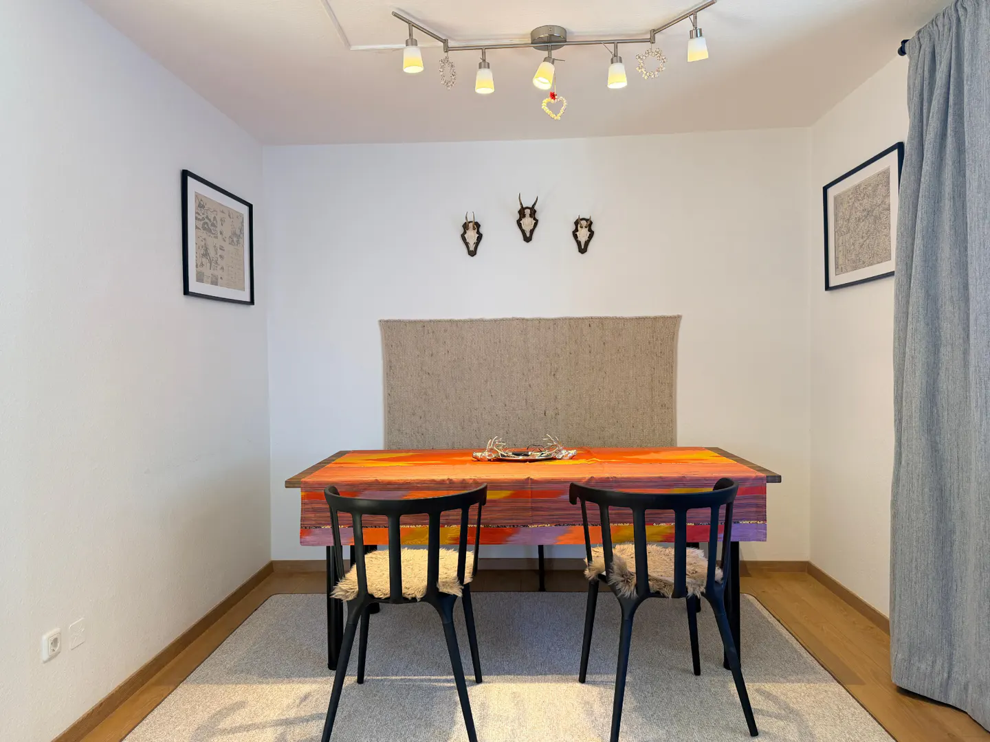 A dining room with a colorful table, black chairs with fur cushions, and animal skull decorations on the white wall.