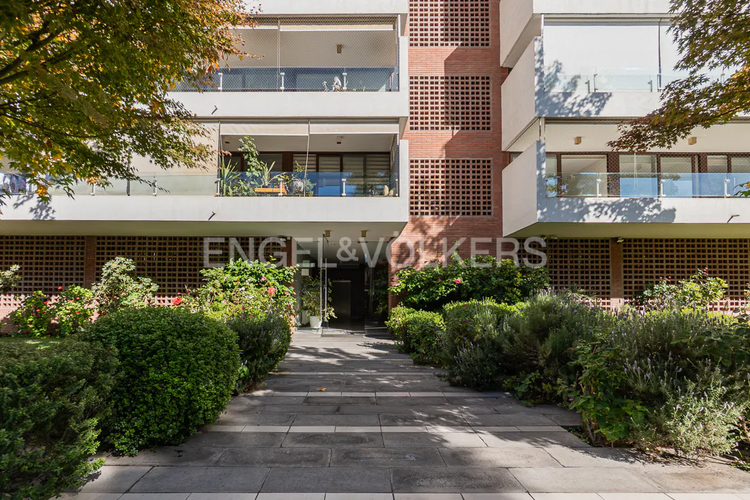 Exterior view of a modern apartment building with balconies, brick accents, and lush green landscaping. "Engel & Volkers" logo displayed.