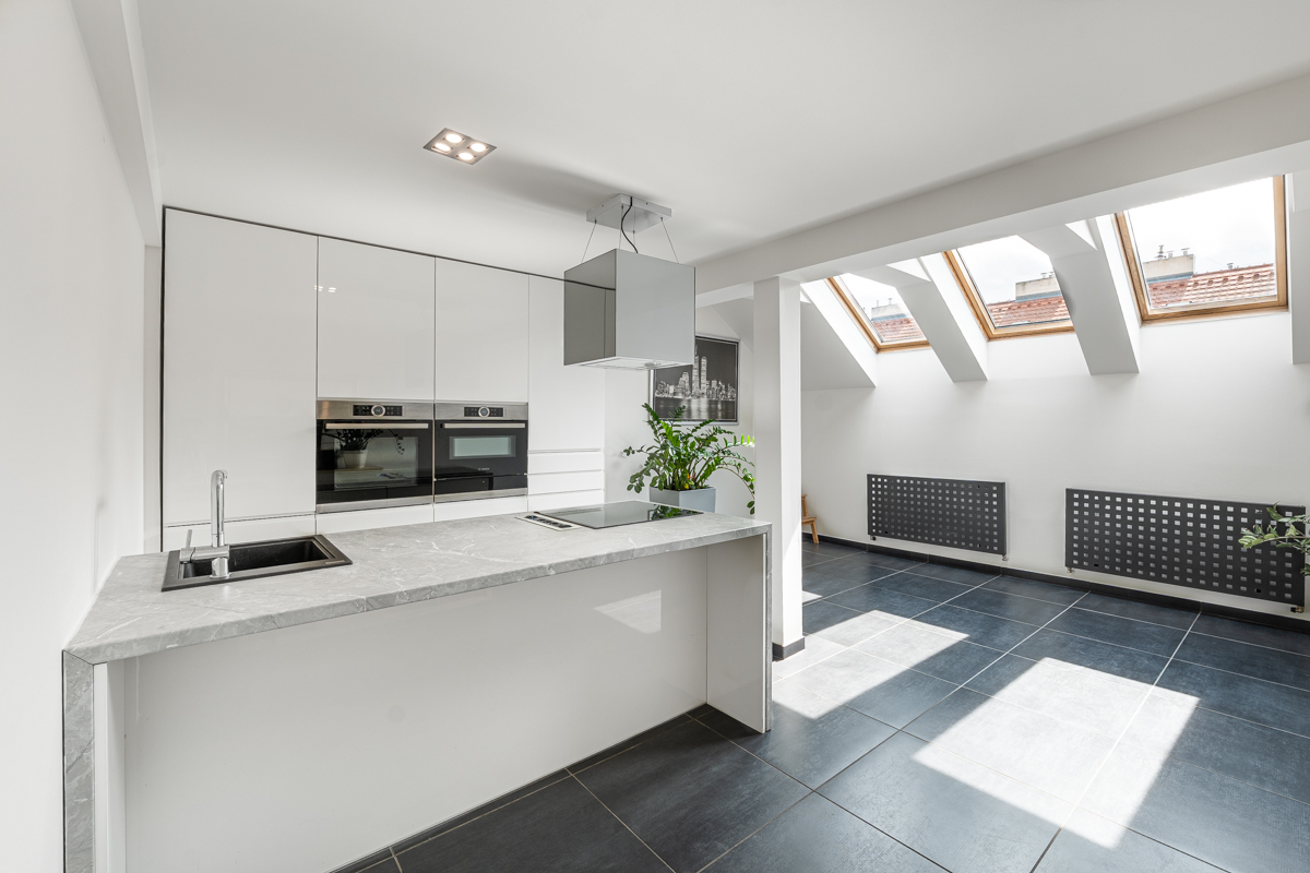 Modern white kitchen with marble island, dark tile floors, and skylights in a bright, open-plan attic space. [AI-generated text]