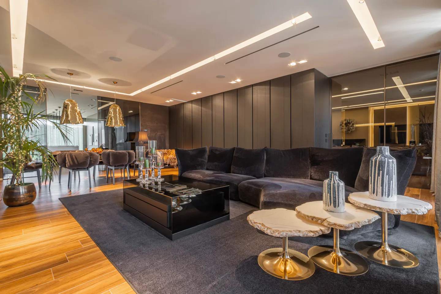 A modern living room with a black sectional sofa, black coffee table, and three small round tables. The walls are dark, and the floor is light wood.