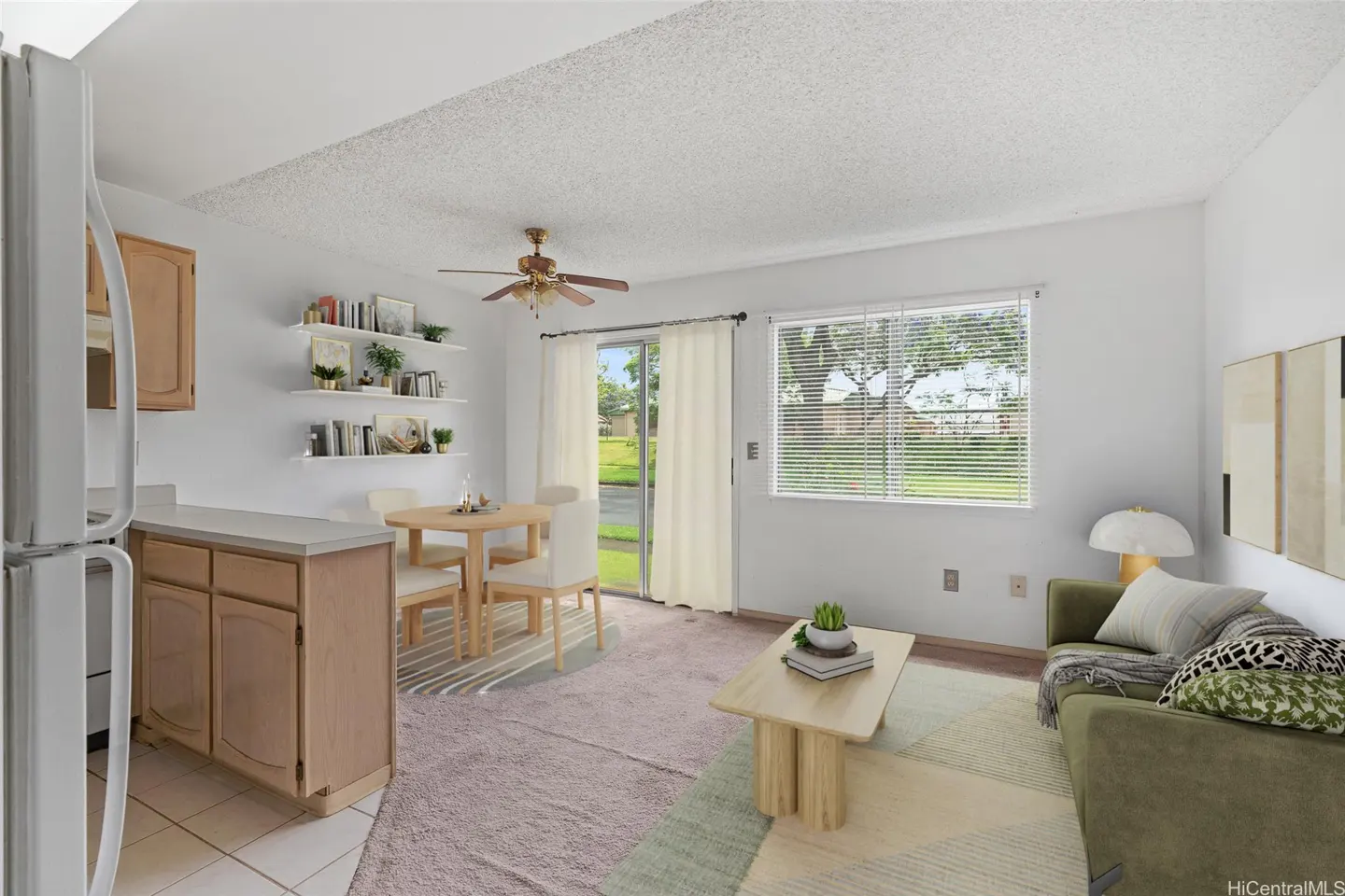Bright living space with white walls, wood cabinets, and a dining table. A green sofa and coffee table sit on a geometric rug.