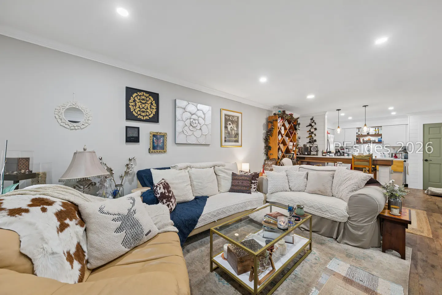 Living room with tan leather sofa, white sofas, glass coffee table, and art on the gray walls. Open kitchen in the background.