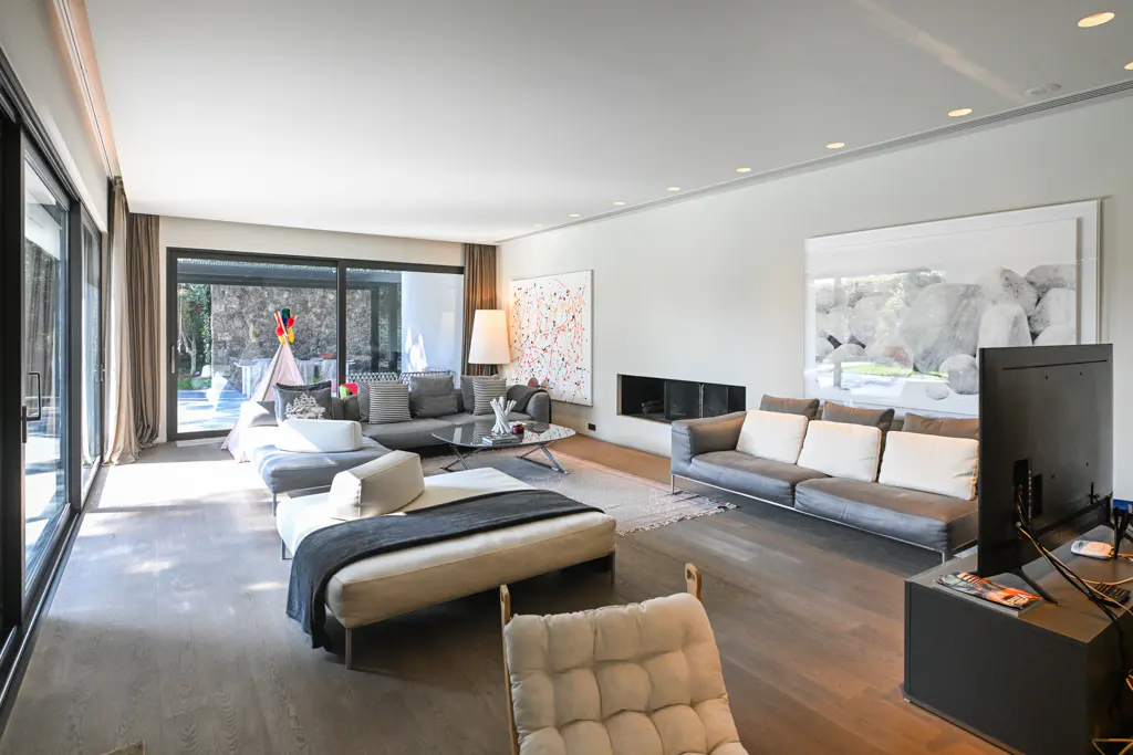 Bright living room with gray sofas, white cushions, and a black TV. A teepee is visible through the glass doors.
