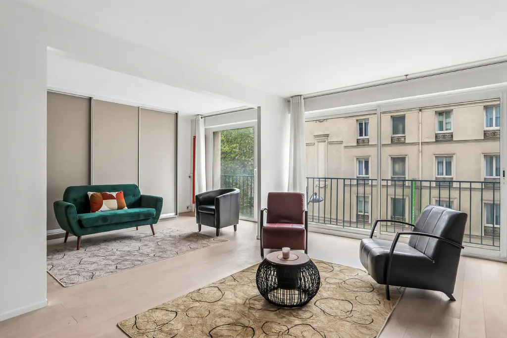Bright living room with a green sofa, black and brown chairs, and a balcony overlooking a building.