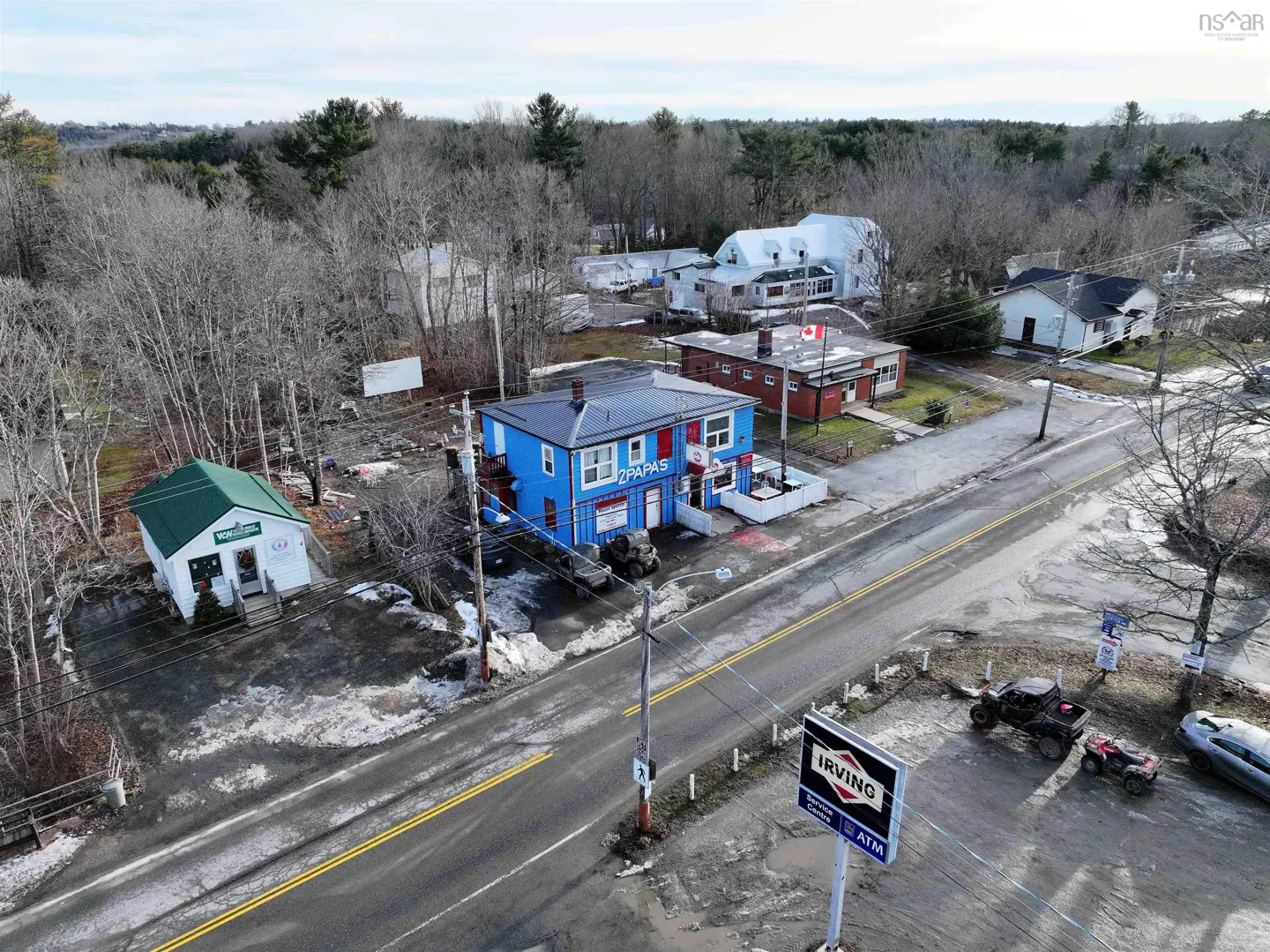 Aerial view of a rural street with a blue "2 Papas" building, an Irving gas station sign, and scattered snow.