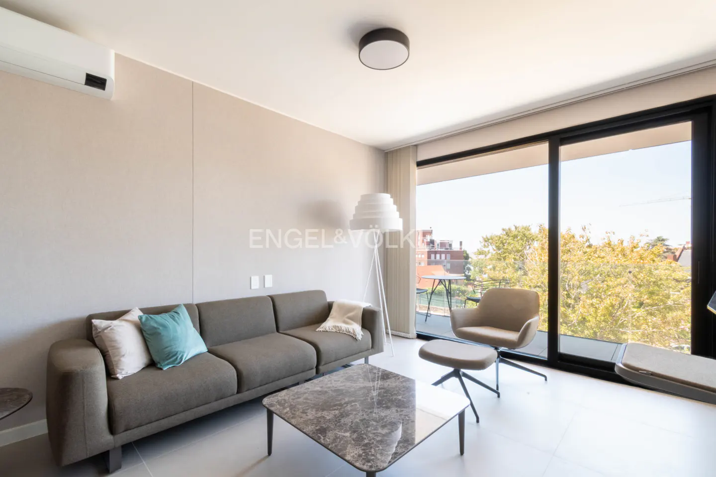 Living room with gray sofa, marble table, and chair near a large window with a view of trees and buildings.