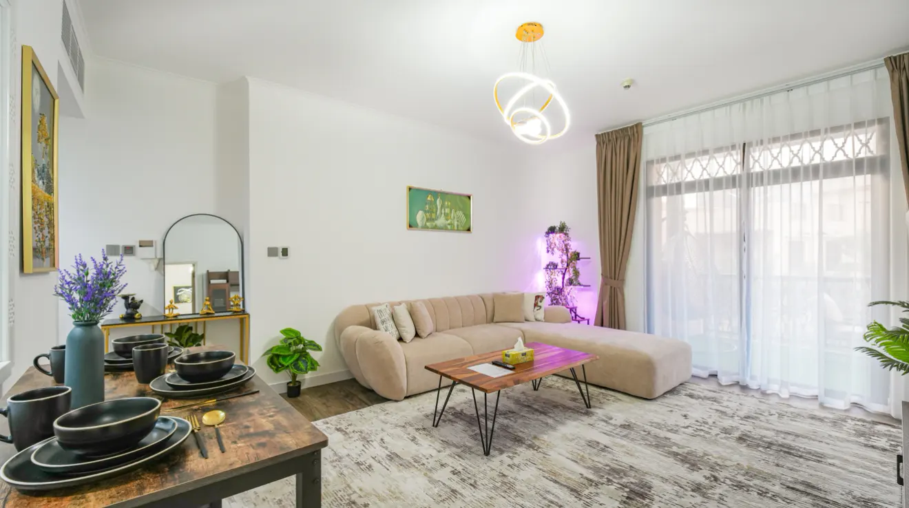 A bright living room with a beige sectional sofa, a wooden coffee table, and a dining table set for a meal.