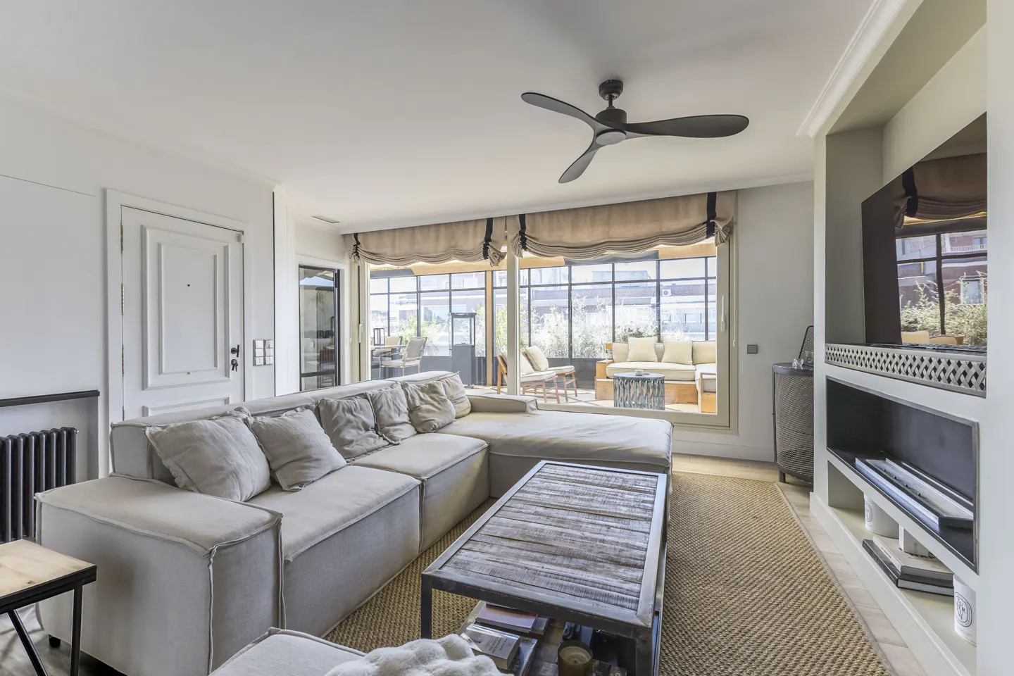 Bright living room with a large sectional sofa, rustic coffee table, and floor-to-ceiling windows leading to a patio.
