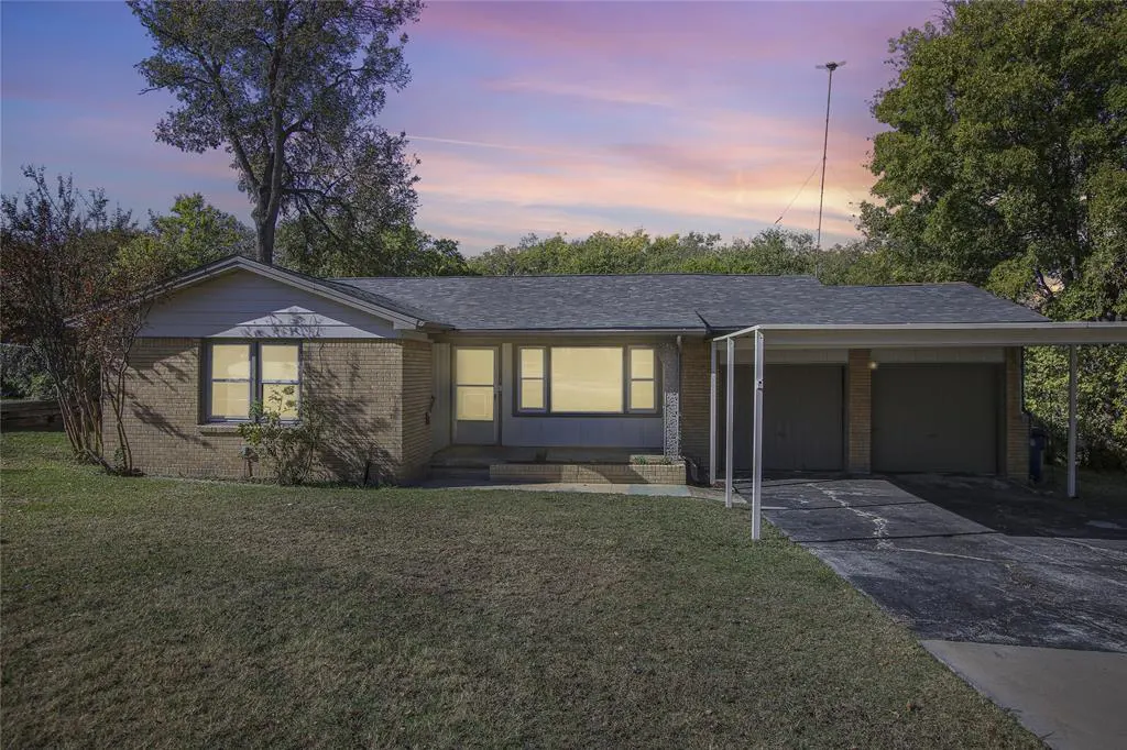 A single-story brick house with a two-car carport at dusk. The sky is pink and purple.