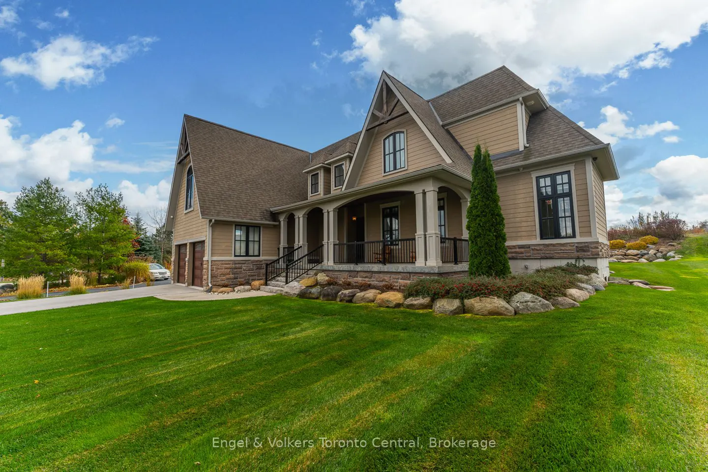 Tan two-story house with a covered porch, stone accents, and a green lawn under a blue sky.