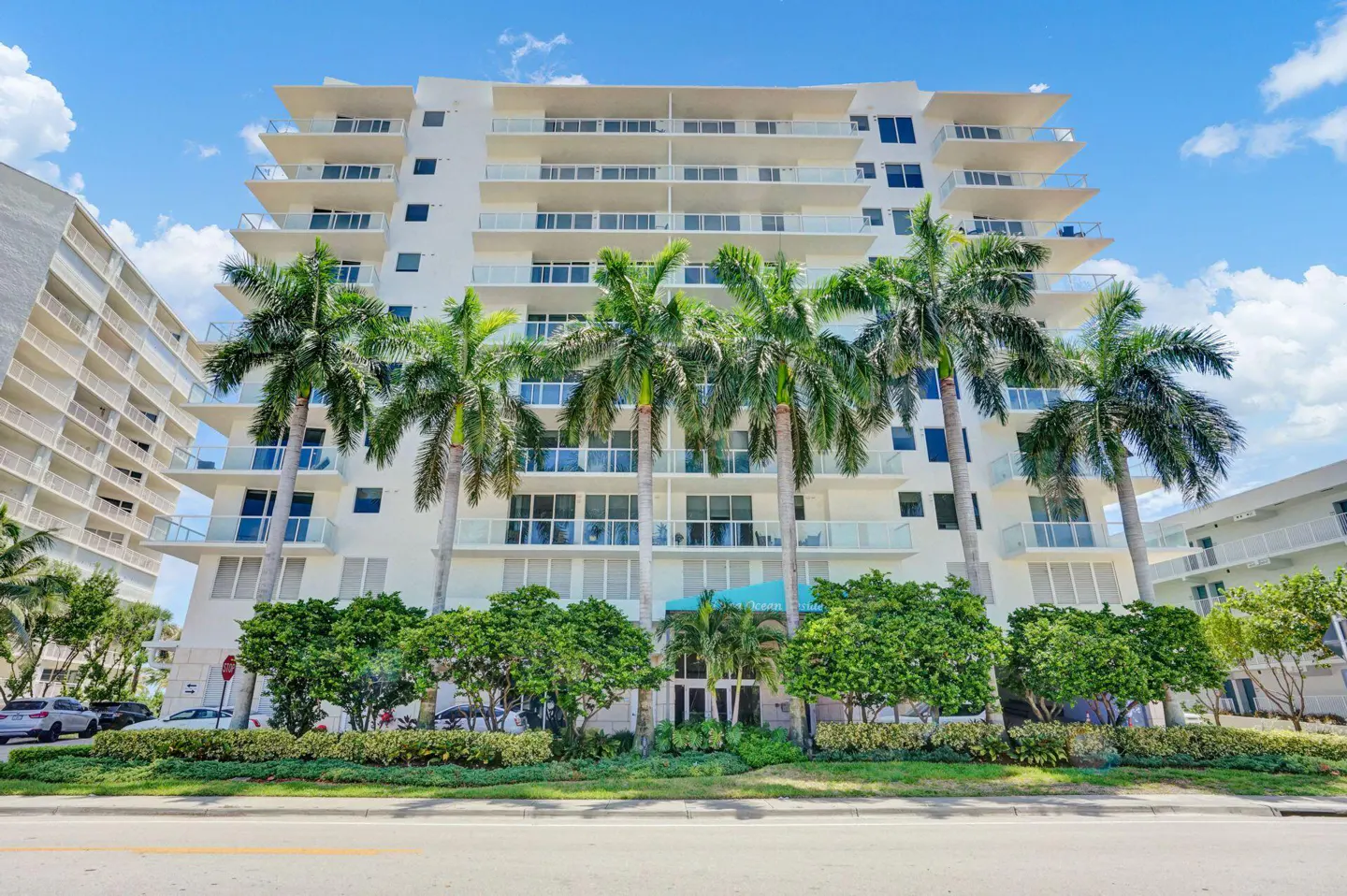 A white, multi-story condo building with palm trees in front, under a blue sky.