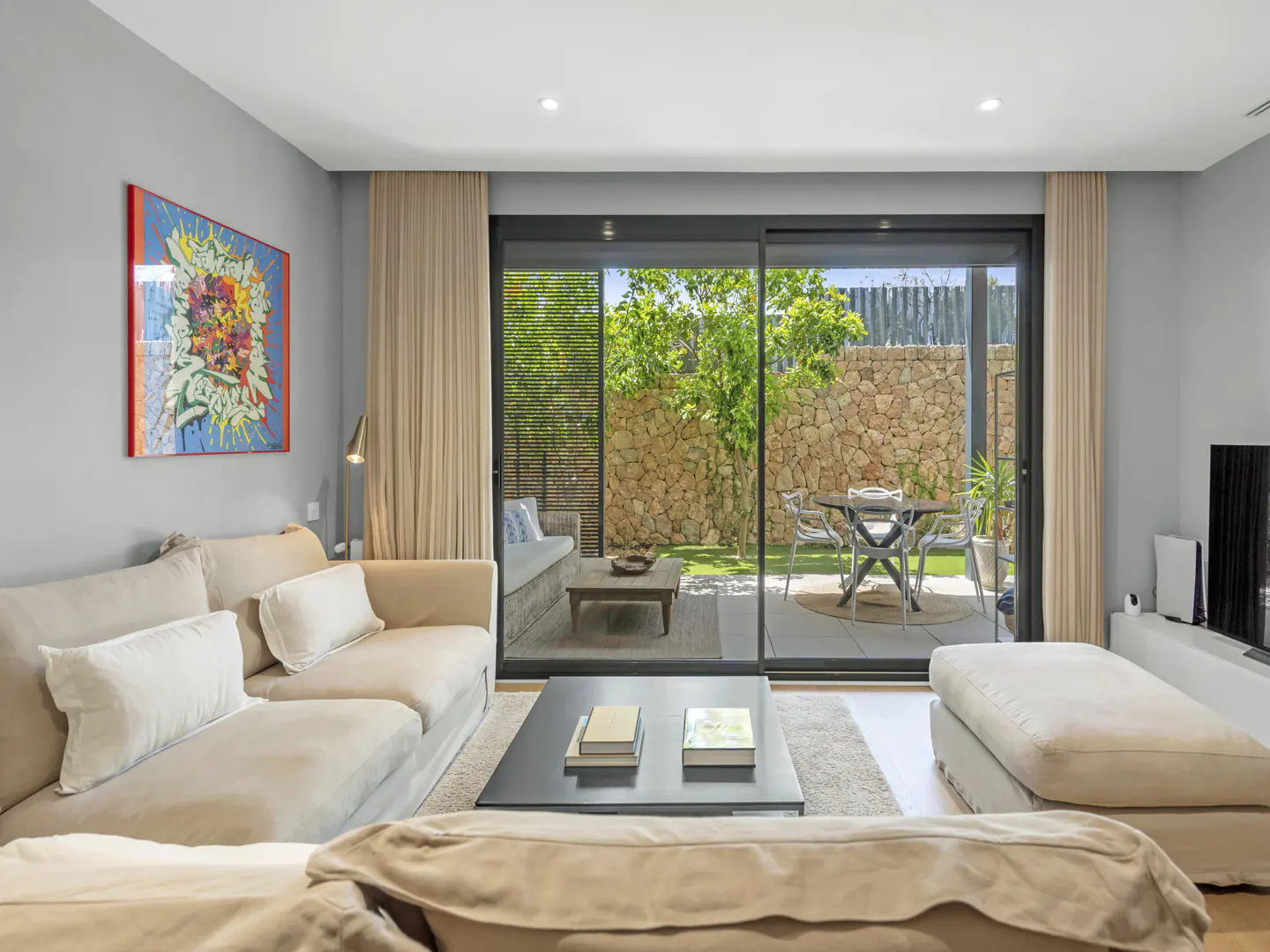 Living room with beige sofas, a black coffee table, and sliding glass doors to a patio with a stone wall.