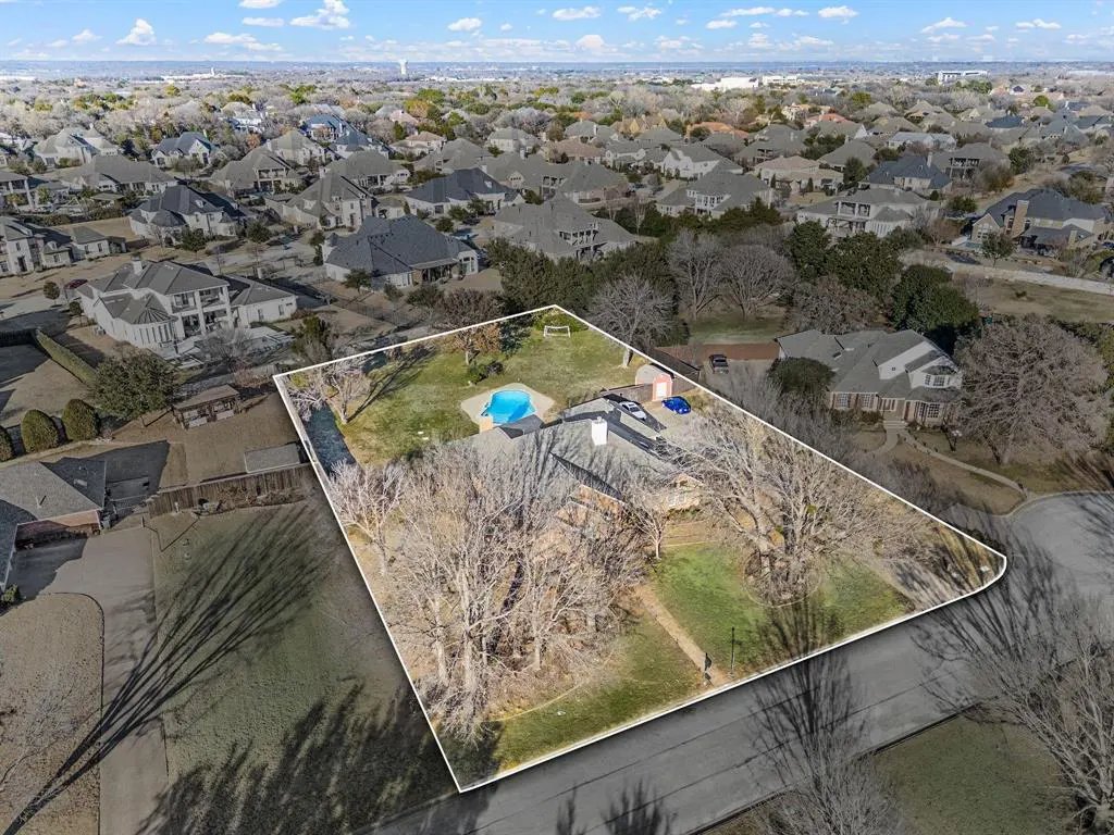 Aerial view of a property outlined in white, featuring a pool, lawn, and trees, surrounded by a neighborhood of similar homes.