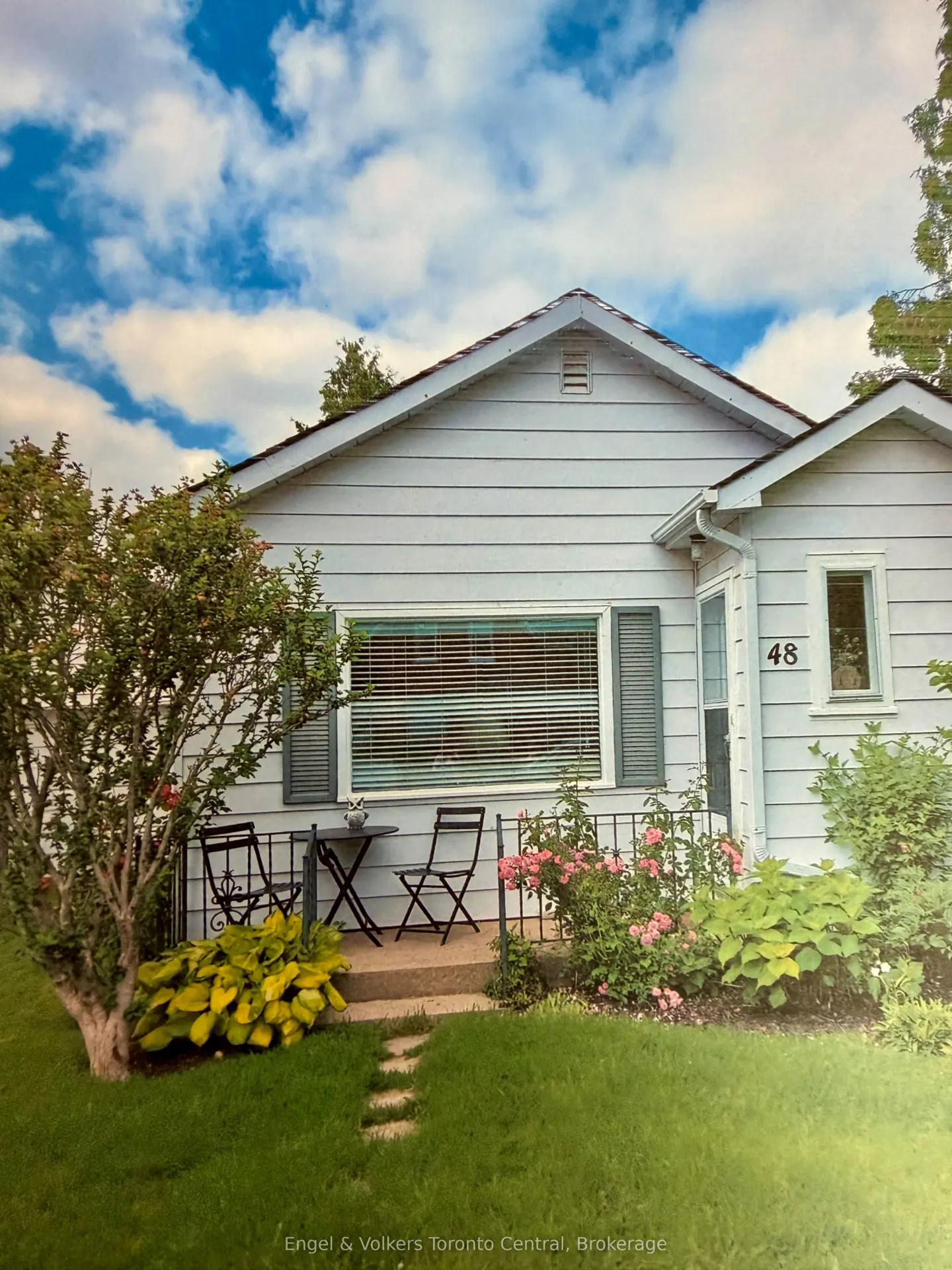 Exterior of a light blue house with a small patio set, flowers, and green lawn.