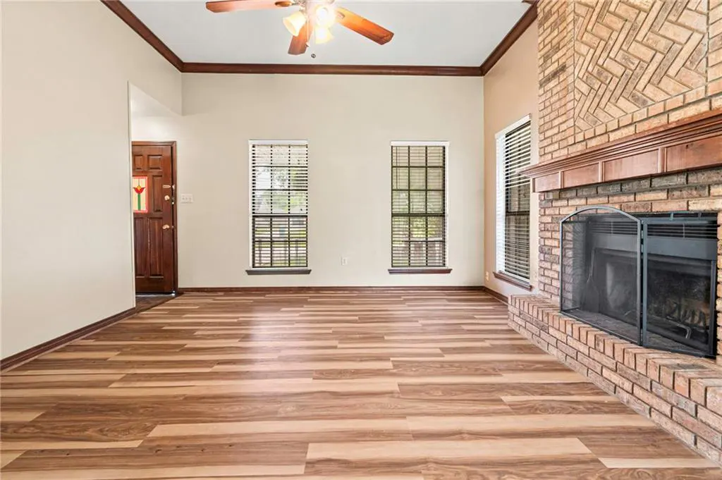 A living room with wood floors, a brick fireplace, and two windows. A ceiling fan is visible.