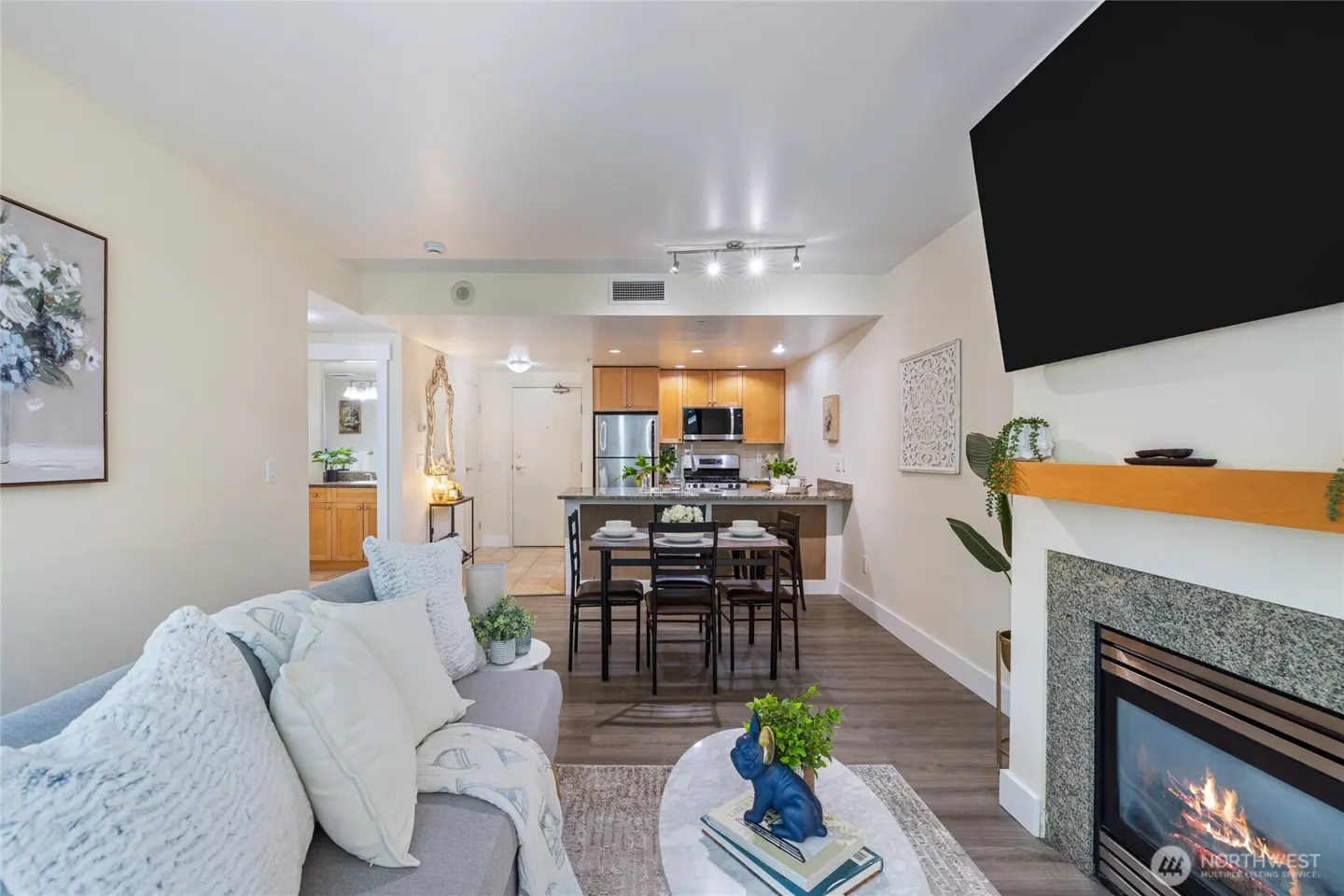 Open-concept living space with a gray sofa, fireplace, dining table, and kitchen with stainless steel appliances.