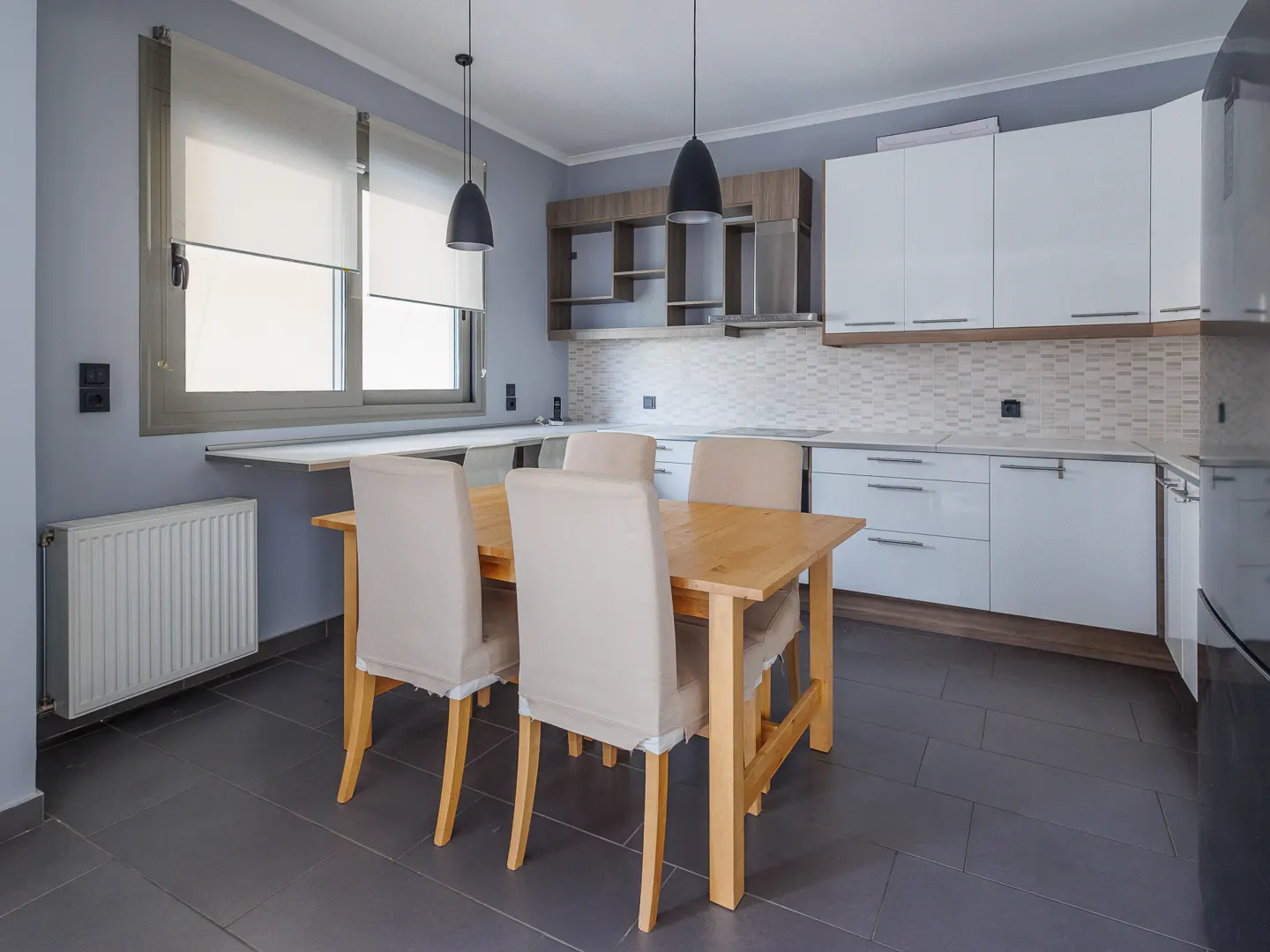A modern kitchen with a wooden table and four beige chairs. White cabinets and gray walls create a clean, bright space.