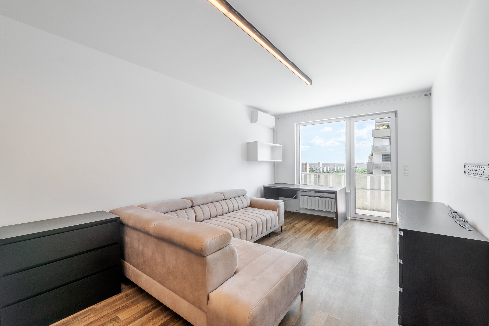 Modern living room with a beige sectional sofa, black furniture, wood floors, and a balcony door with city views.