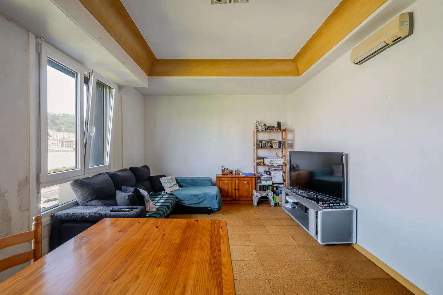 Bright living room with a dark gray sofa, blue chaise lounge, wooden table, TV, and a view from the window.