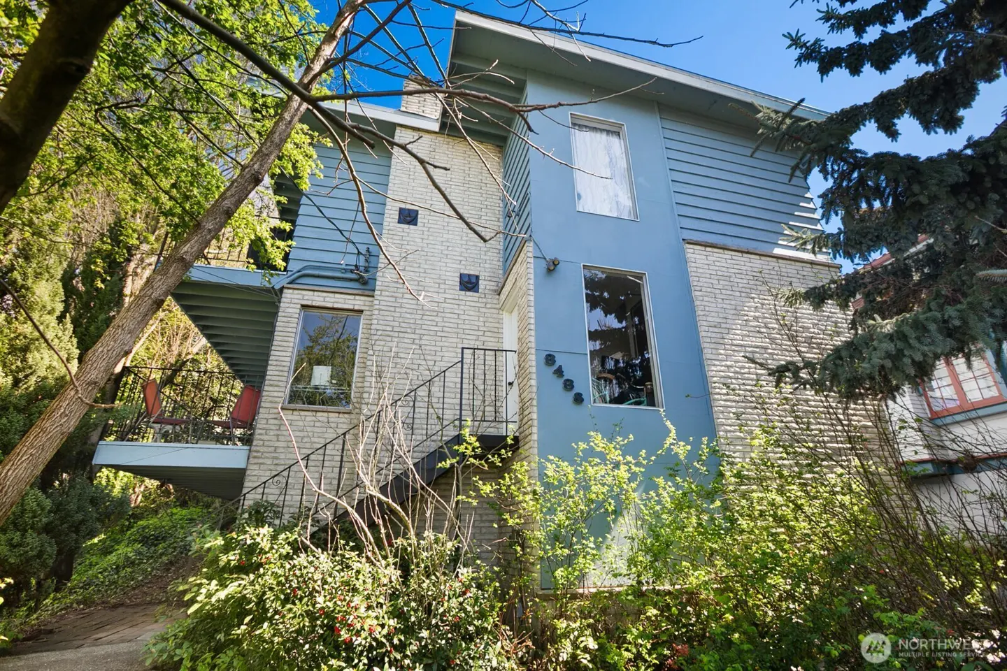 Exterior view of a two-story house with a brick and blue siding, a balcony, and stairs leading to the entrance.