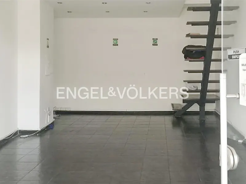 Empty commercial space with dark tile floor, white walls, and black metal stairs. Engel & Völkers logo on the wall.